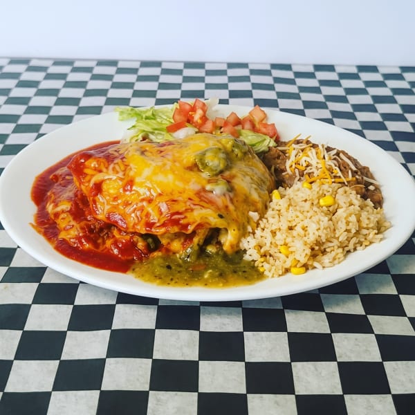 A plate of enchiladas with red and green sauce, rice, beans, and a side salad on a checkered tablecloth.