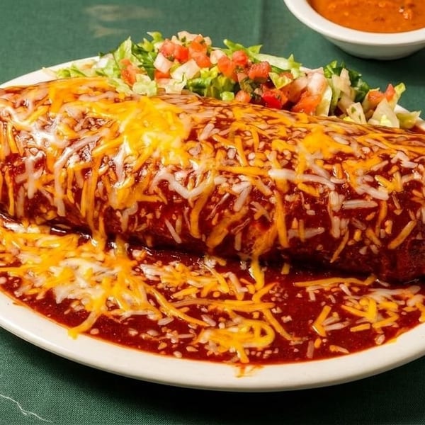 Smothered burrito covered in melted cheese and red sauce, with a side salad and two small bowls of salsa.