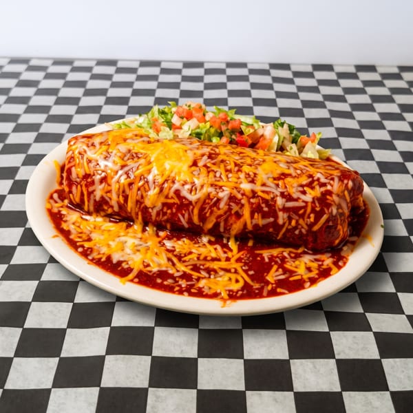 A large, smothered burrito covered in red sauce and melted cheese, with a side of lettuce and pico de gallo.