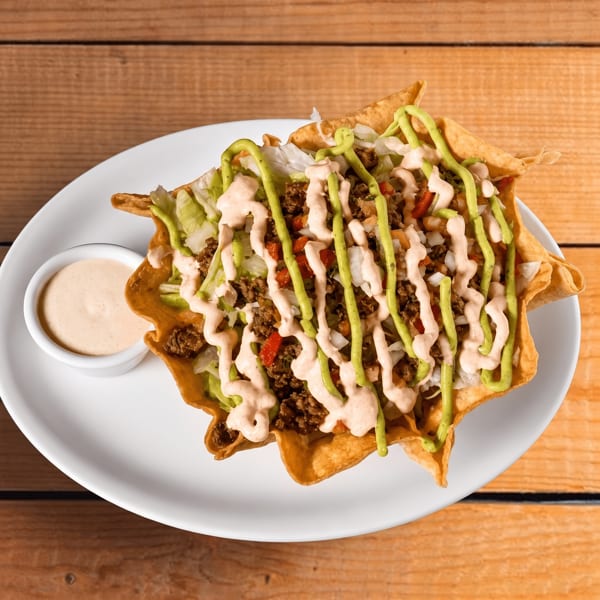 A taco salad in a crispy tortilla bowl, topped with ground beef, lettuce, and two sauces.